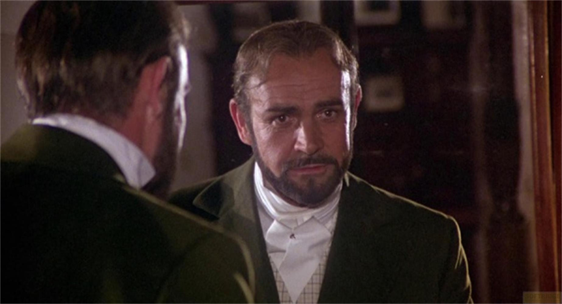Un uomo barbuto indossa un abito scuro e una camicia bianca.