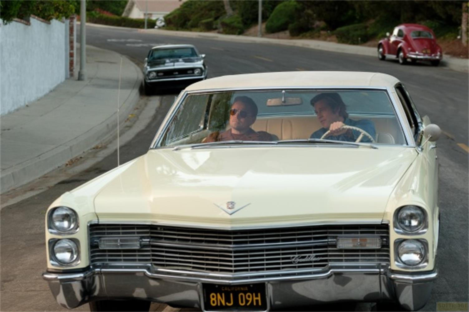 Una Cadillac color crema guida su una strada, due uomini siedono all'interno.