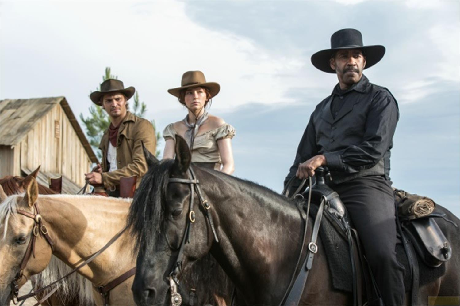 Trois cow-boys montent à cheval devant un bâtiment en bois.