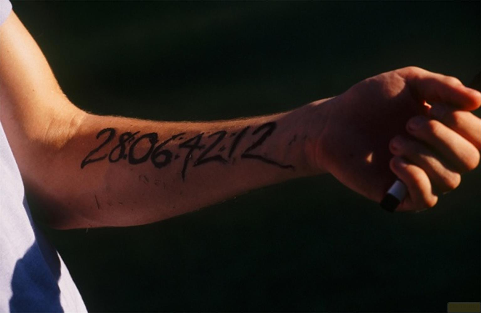 Eine Hand mit der Zahl 28.06.4212 auf dem Unterarm geschrieben, hält einen Stift.