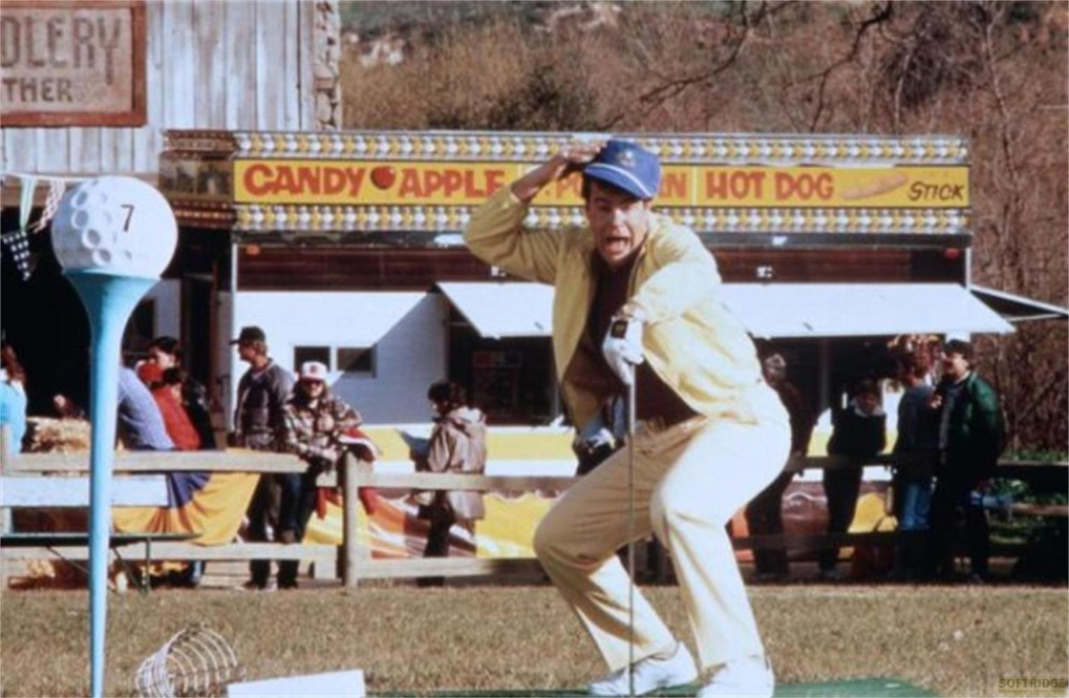 Un uomo con giacca gialla gioca a golf davanti a uno stand "Candy Apple".