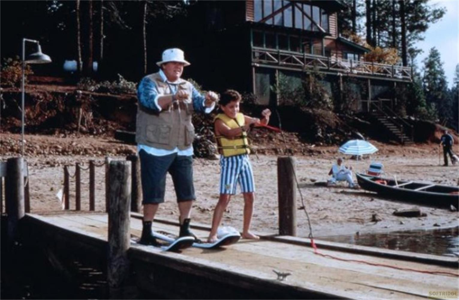Uomo e ragazzo su un molo per sci d'acqua. Casa e spiaggia sullo sfondo.