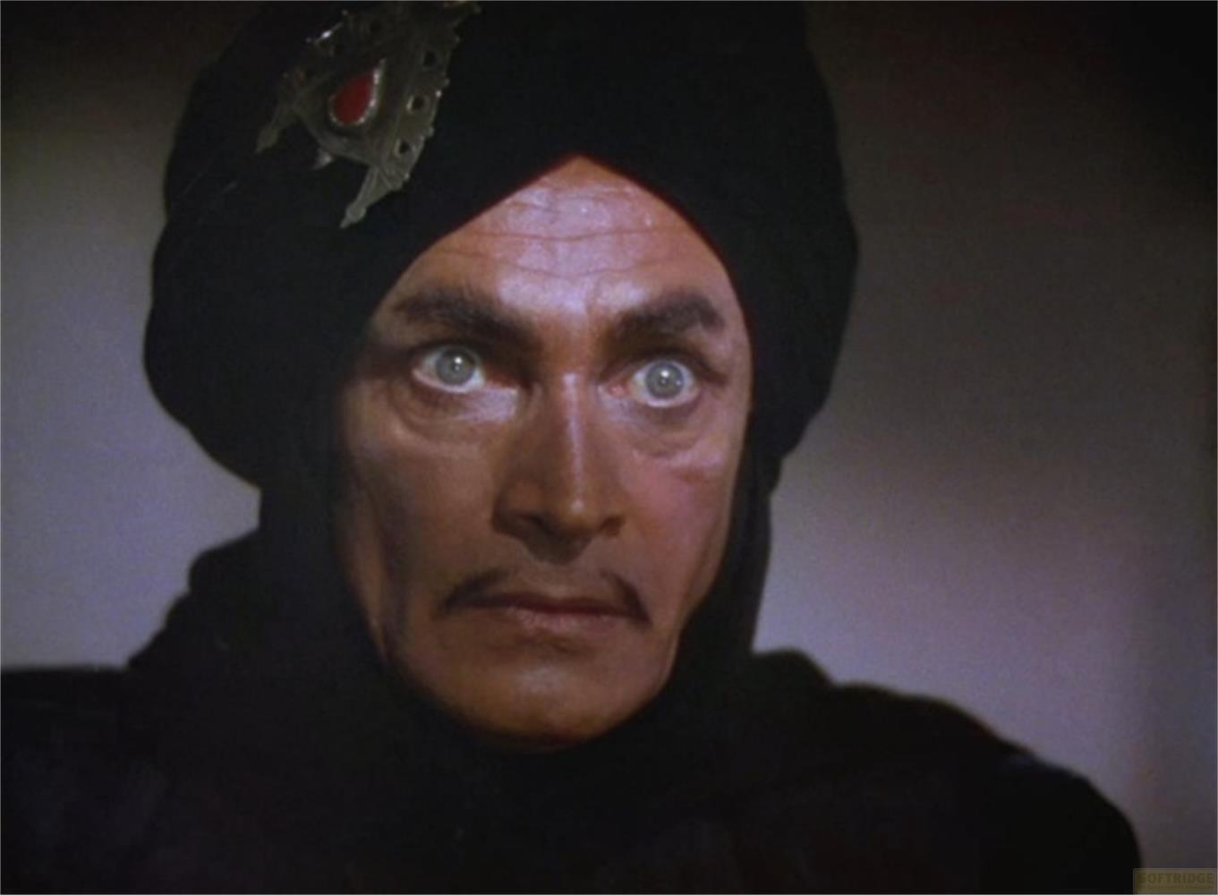Un uomo con turbante nero e gioiello rosso indossa abiti scuri.