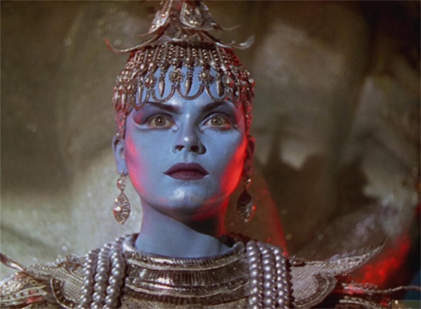 Una donna dalla pelle blu indossa un copricapo e gioielli ornati.