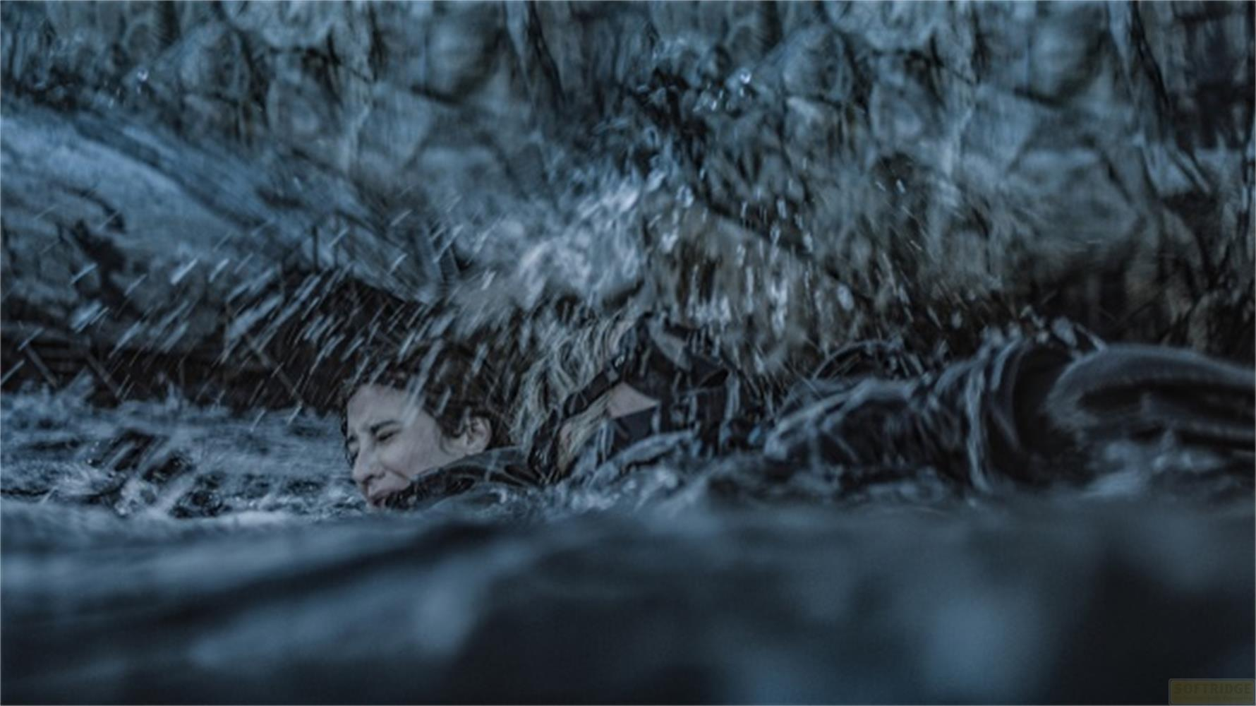 Una donna lotta nell'acqua, circondata da rocce e schizzi.