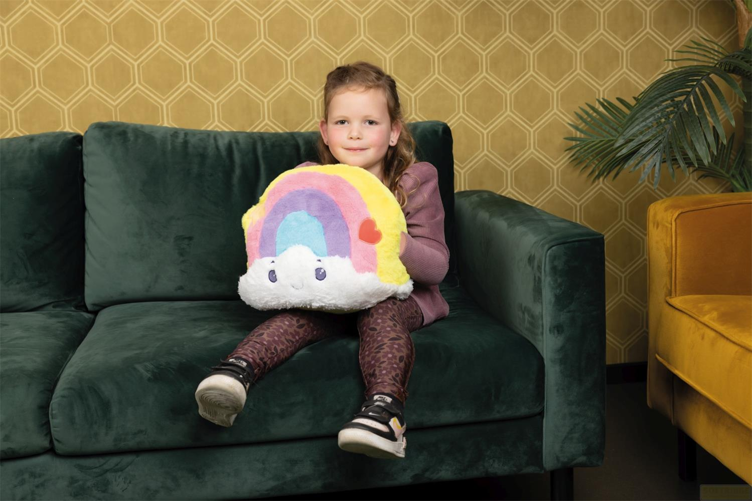 Ein Mädchen sitzt auf einem Sofa und hält ein buntes Regenbogen-Kissen.