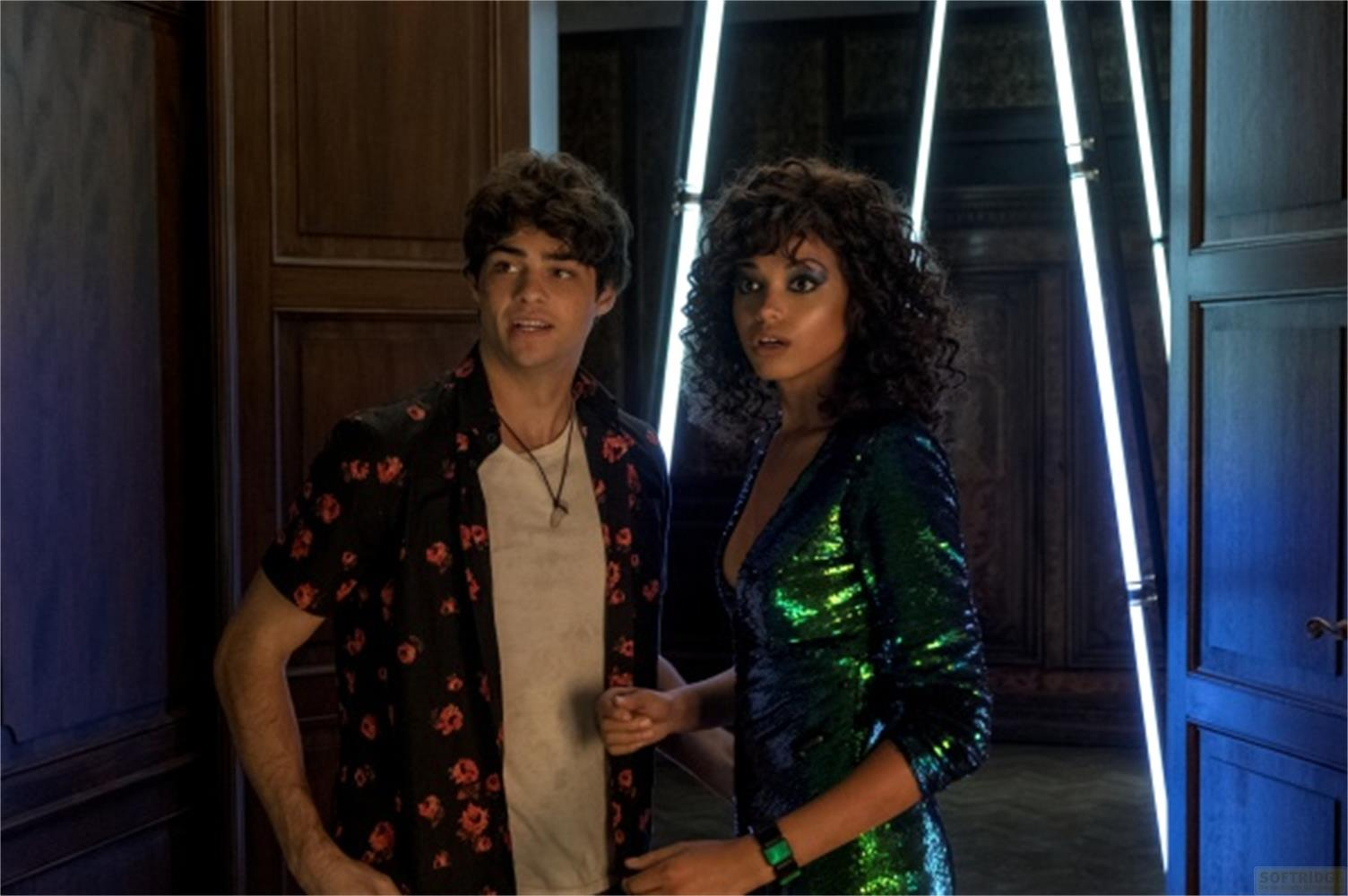 Uomo in camicia floreale e donna in abito di paillettes davanti a tubi neon.