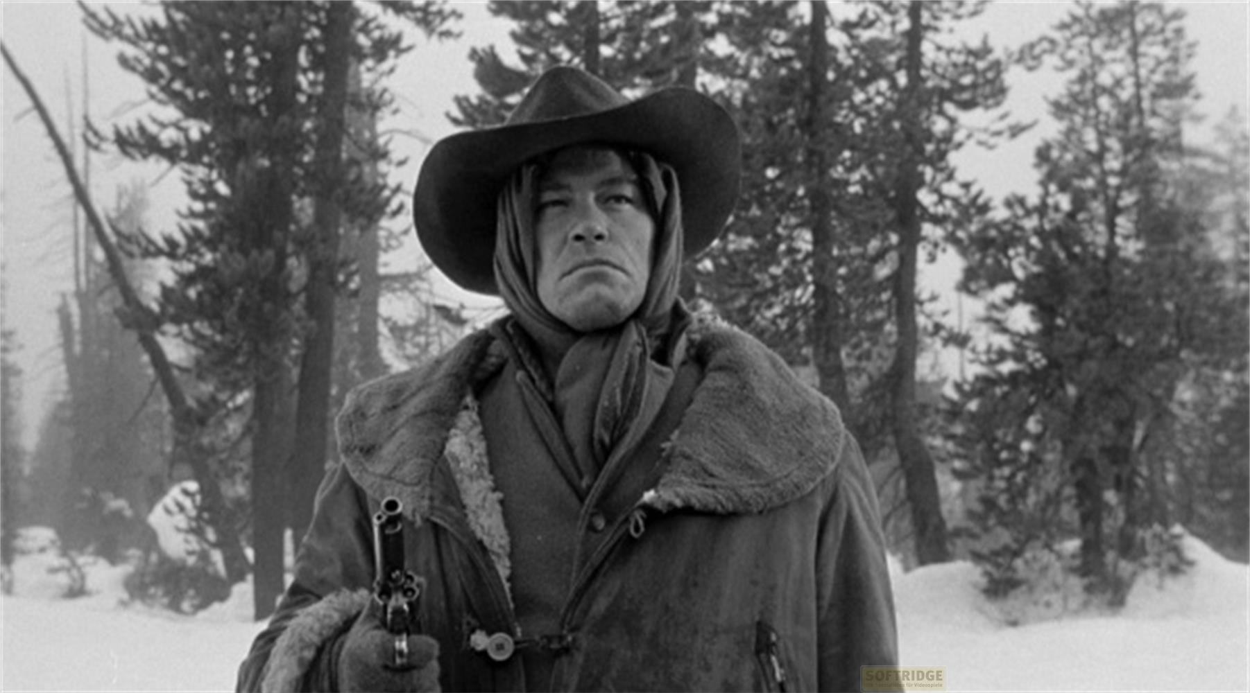 Ein Mann im Cowboyhut und Mantel hält eine Waffe in verschneiter Landschaft.