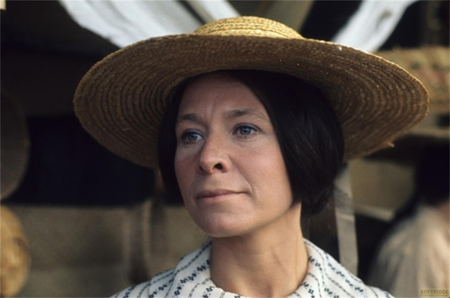 Una donna con capelli scuri corti indossa un cappello di paglia e un top a righe.