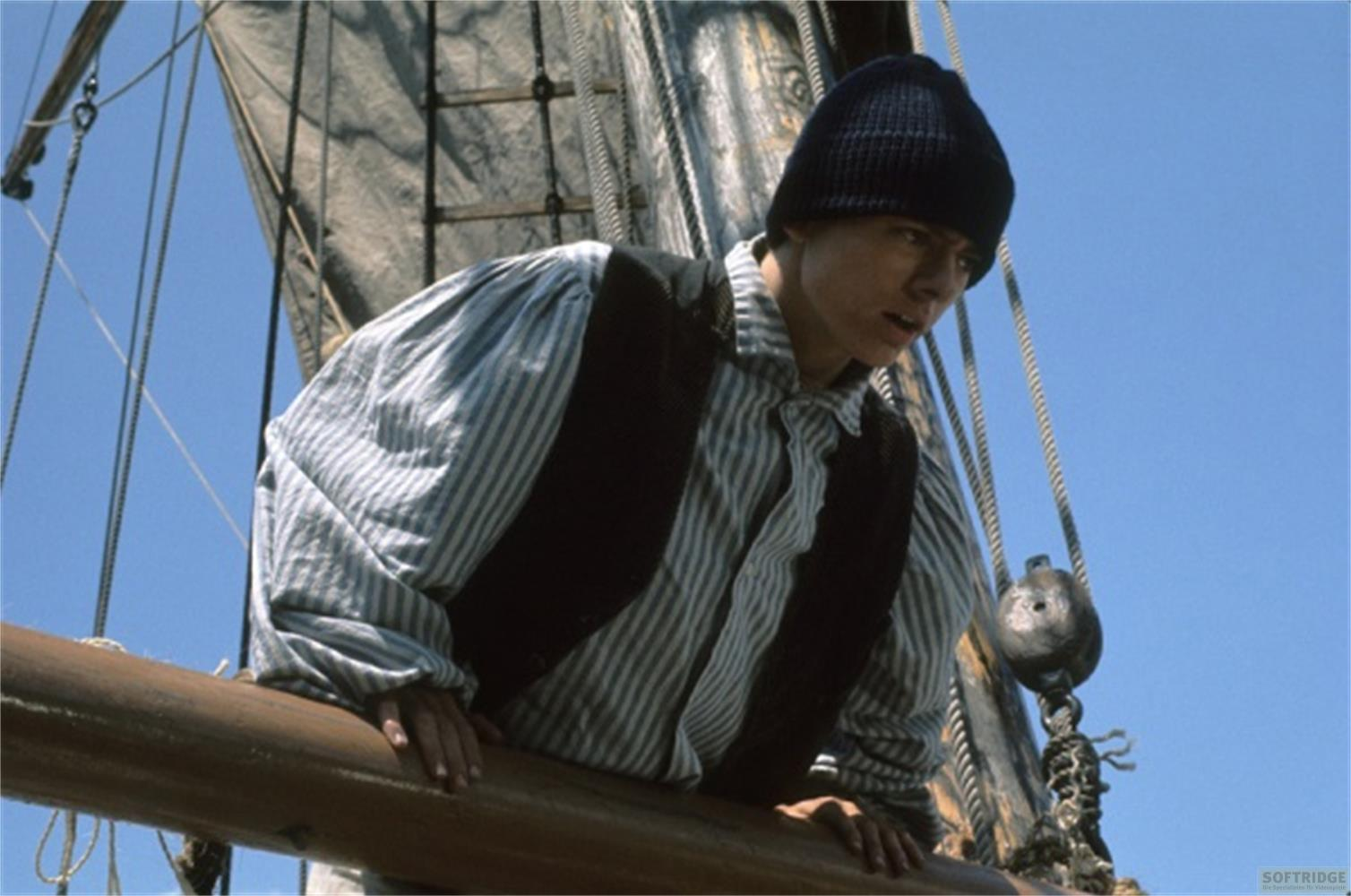 Un ragazzo con berretto e camicia a righe su una barca a vela, che guarda fuori.