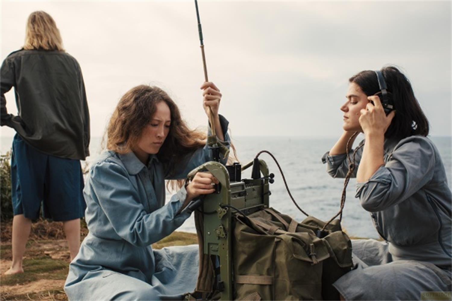Tre donne vicino a una radio al mare. Una ascolta, l'altra la usa.