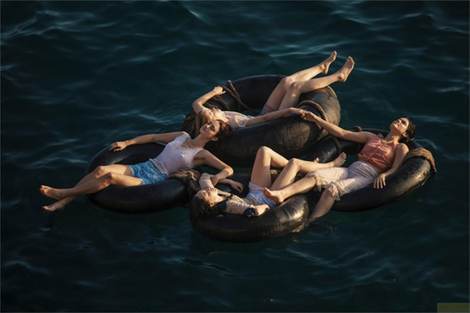 Quattro donne galleggiano su ciambelle in acqua scura, sdraiate rilassate.