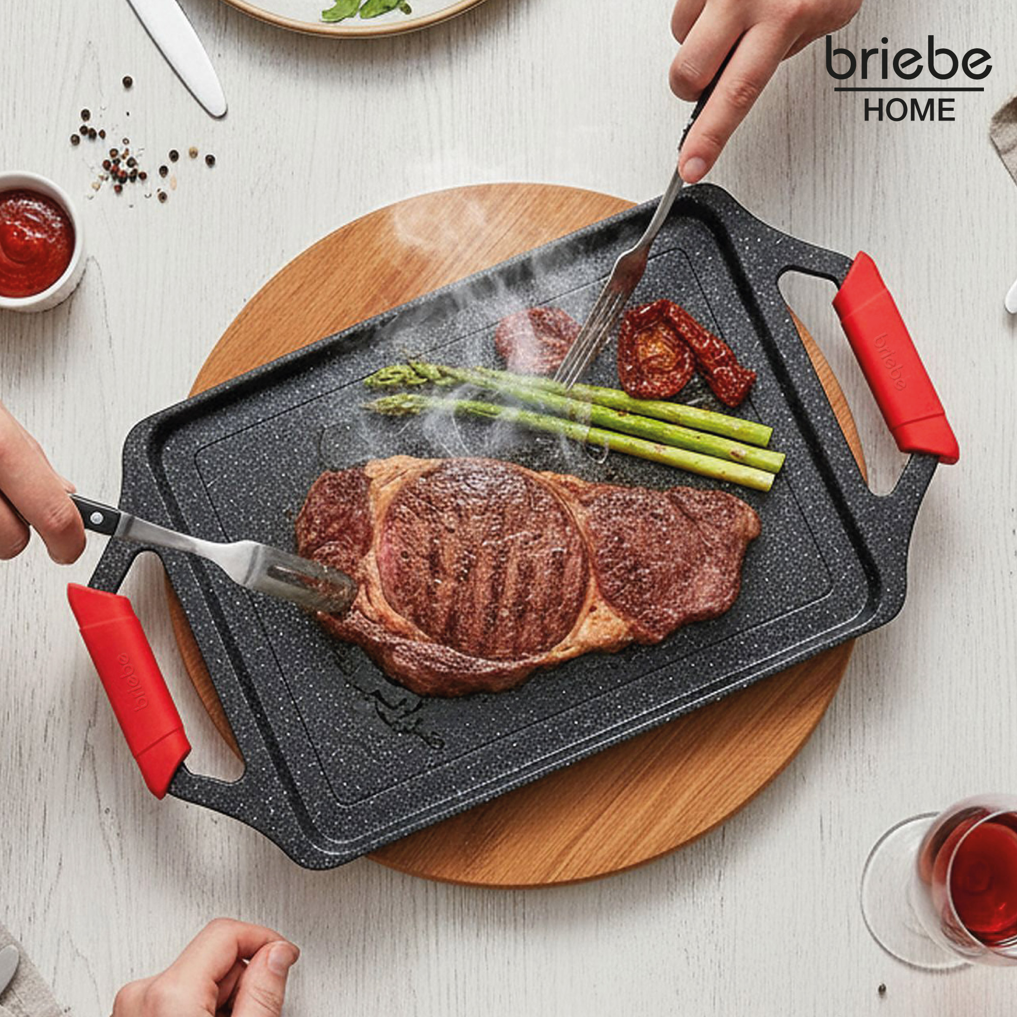 Un filete se asa con espárragos y tomates en una parrilla con asas rojas.