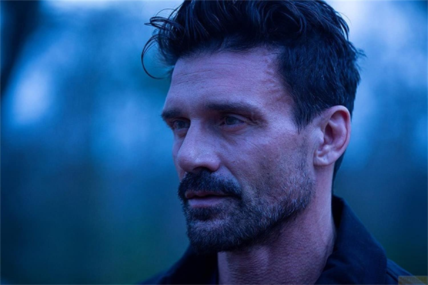 Uomo con capelli scuri e barba, di profilo, sfondo blu.