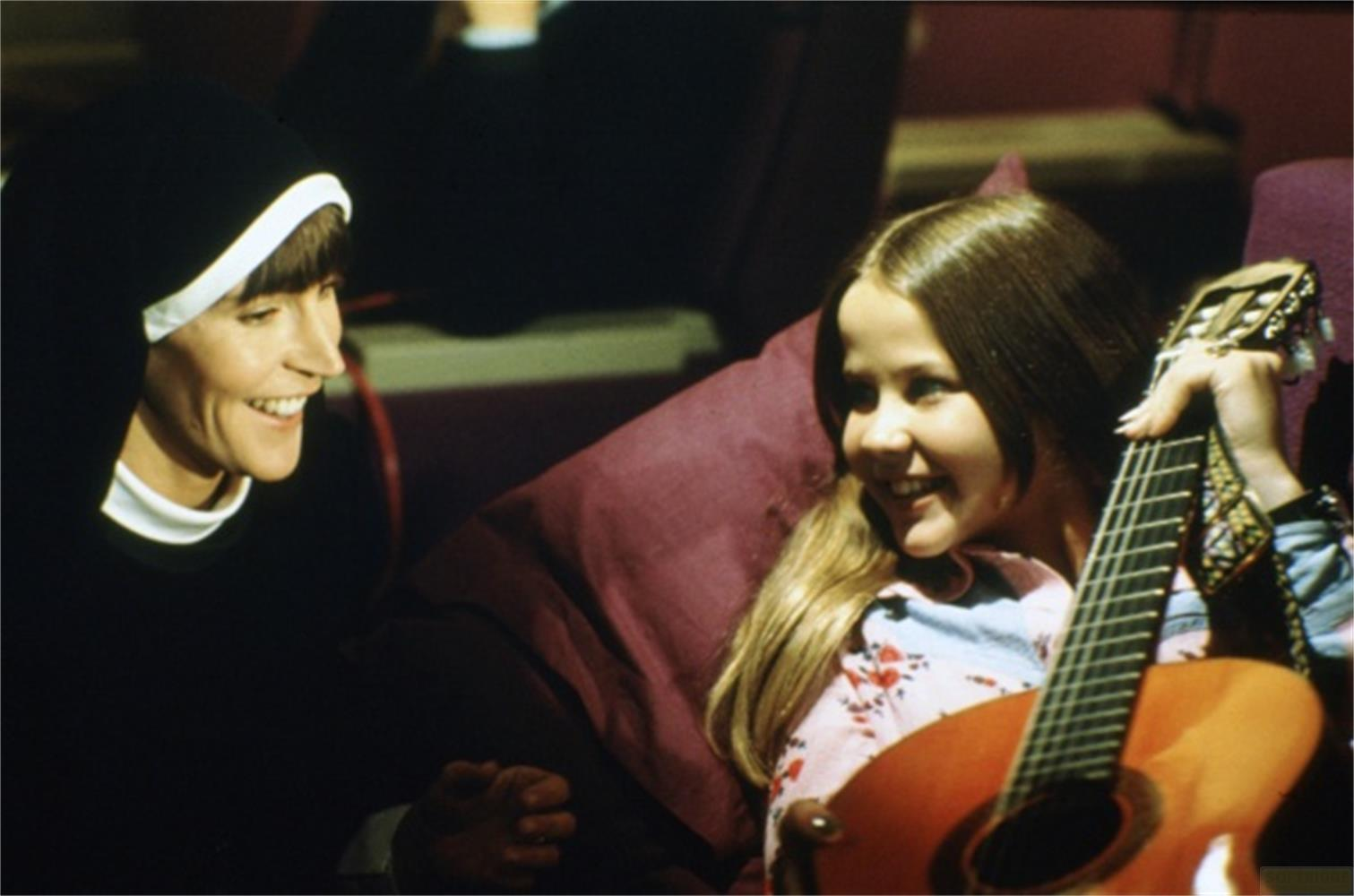 Eine Nonne und ein Mädchen mit Gitarre lachen.