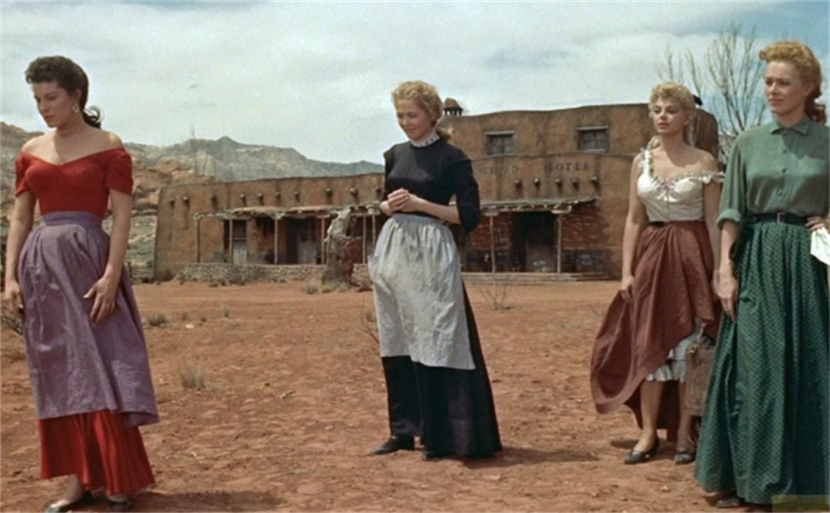 Quattro donne in abiti lunghi davanti a un edificio in stile western.
