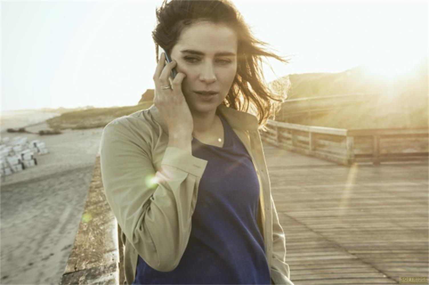 Donna al telefono in spiaggia su passerella di legno con sole.