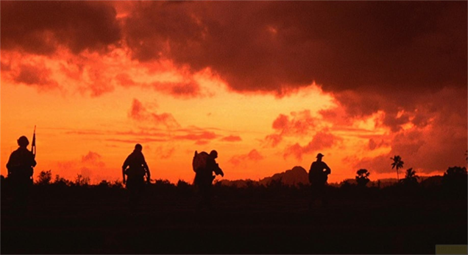Soldats en silhouette devant un coucher de soleil dramatique avec nuages rouges.