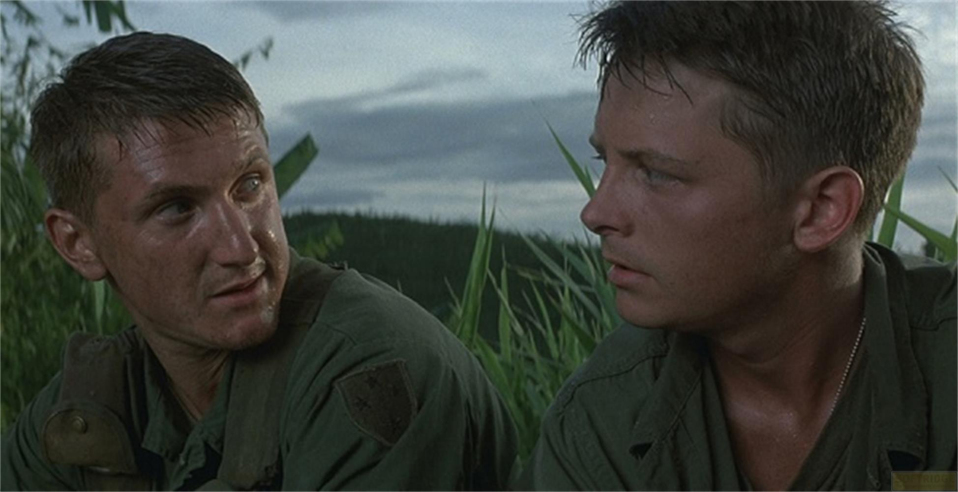 Deux soldats en uniforme vert sont assis dans l'herbe haute sous un ciel nuageux.