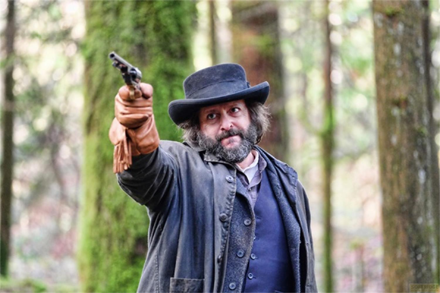 Uomo con cappello e guanti tiene un revolver in una foresta.