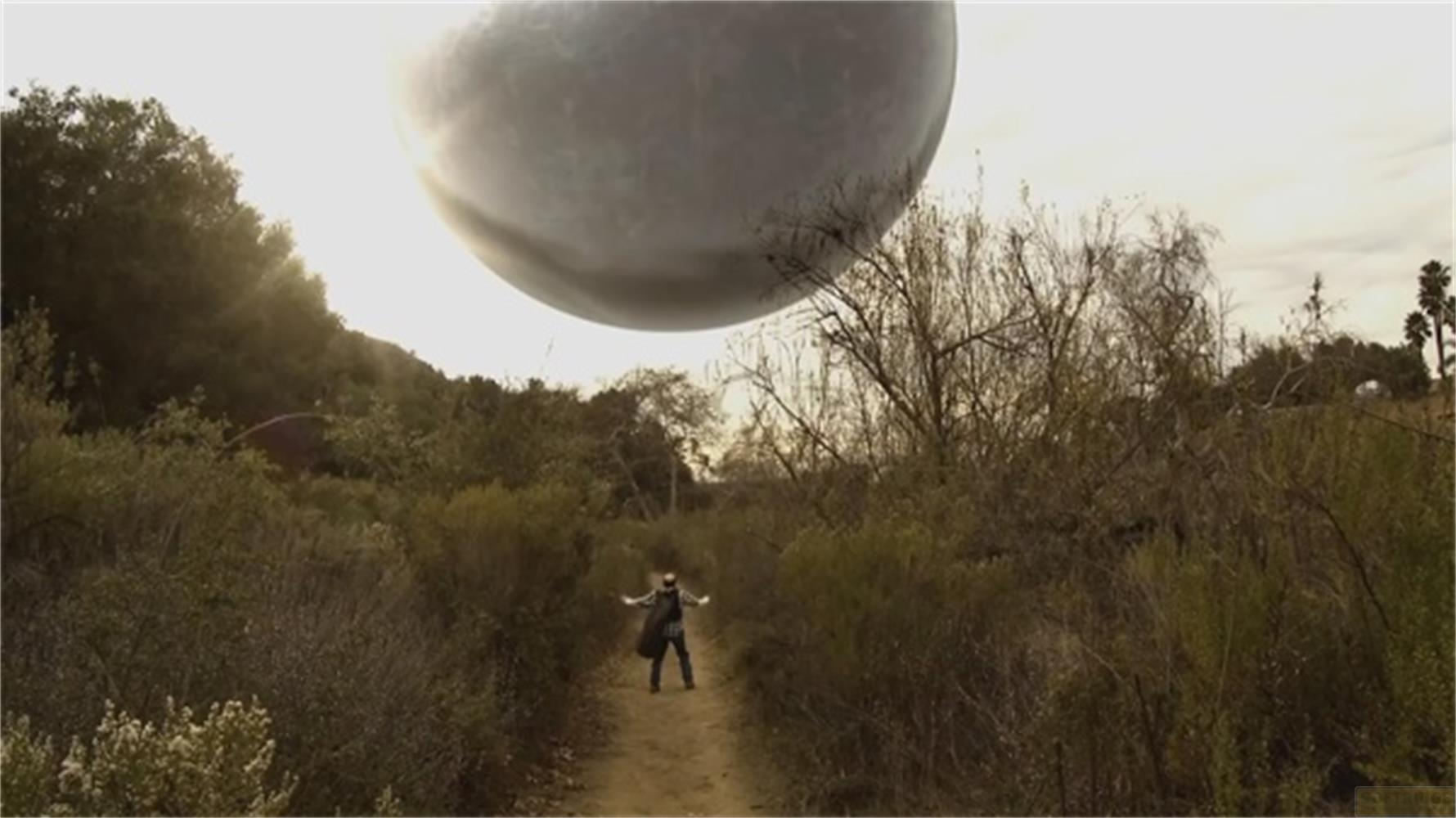 Un uomo sta su un sentiero sotto un gigantesco oggetto grigio nel cielo.