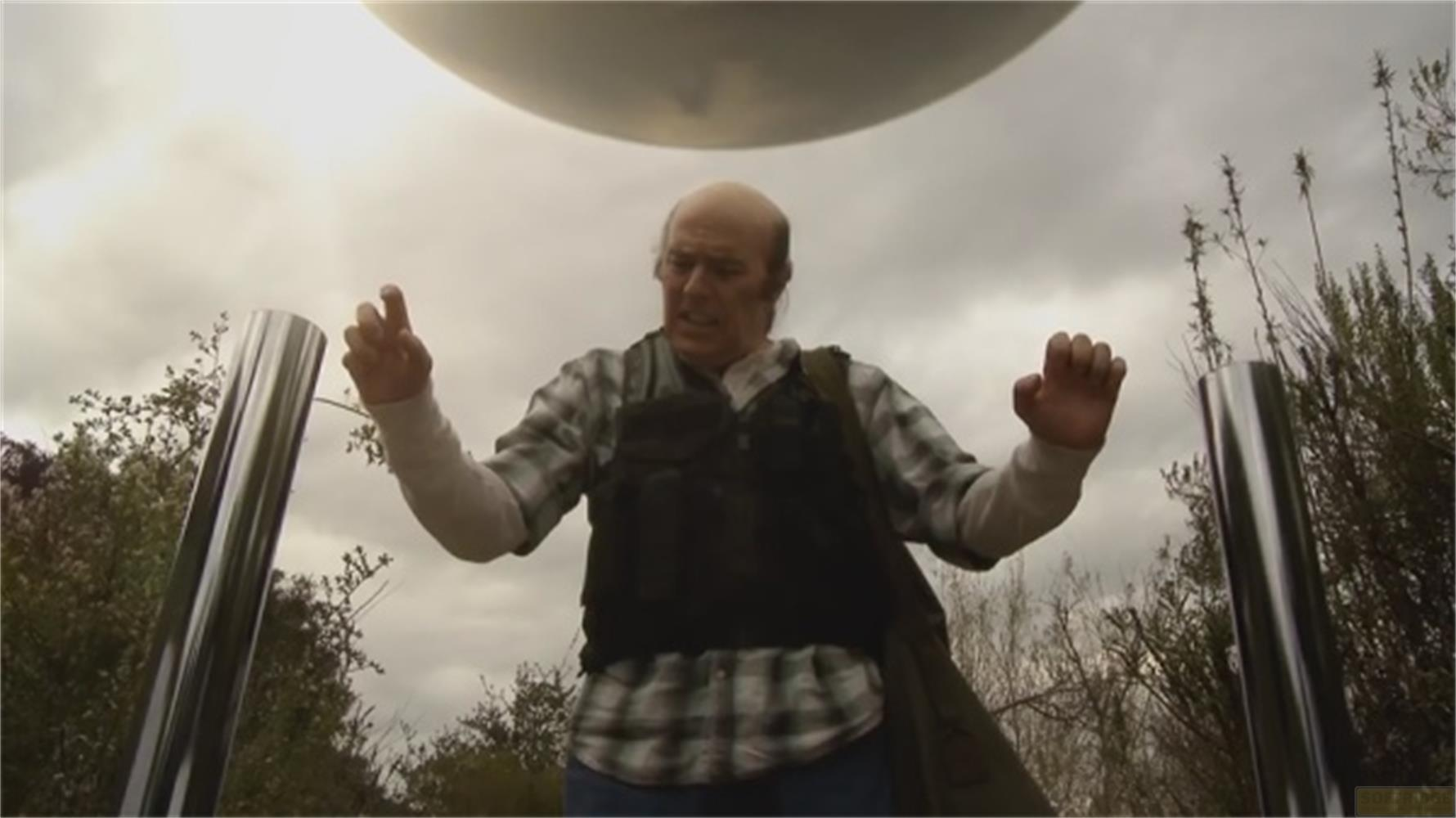 Un uomo con gilet e camicia a quadri sta sotto un UFO all'aperto.