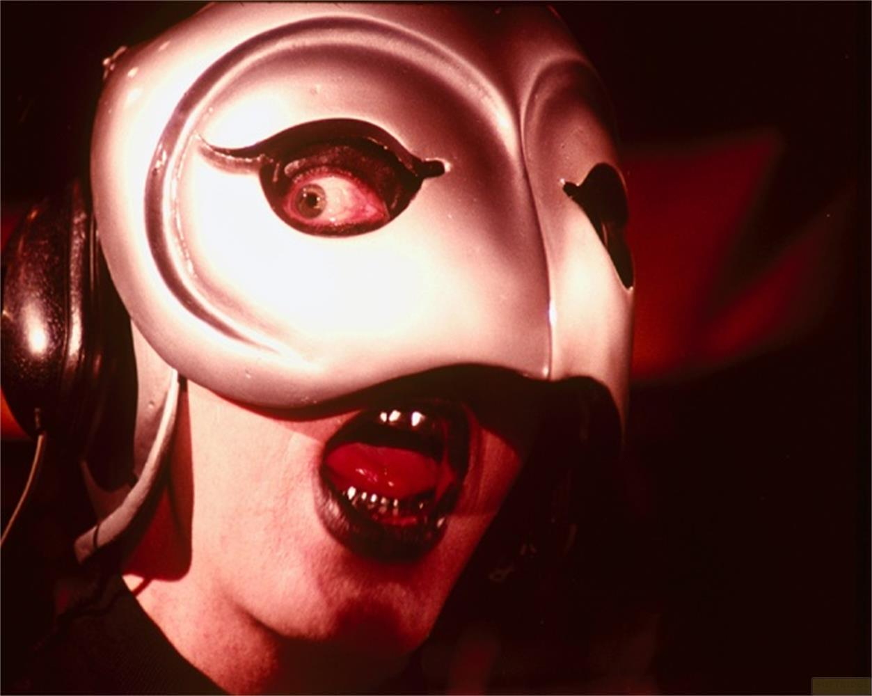 Eine Person mit einer silbernen Maske, Kopfhörern und dunklem Make-up.