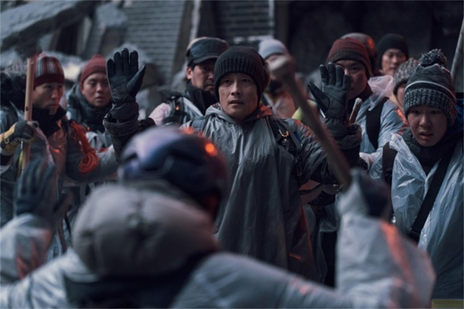 Persone in abiti da esterno e cappelli stanno all'aperto, alcune alzano le mani.