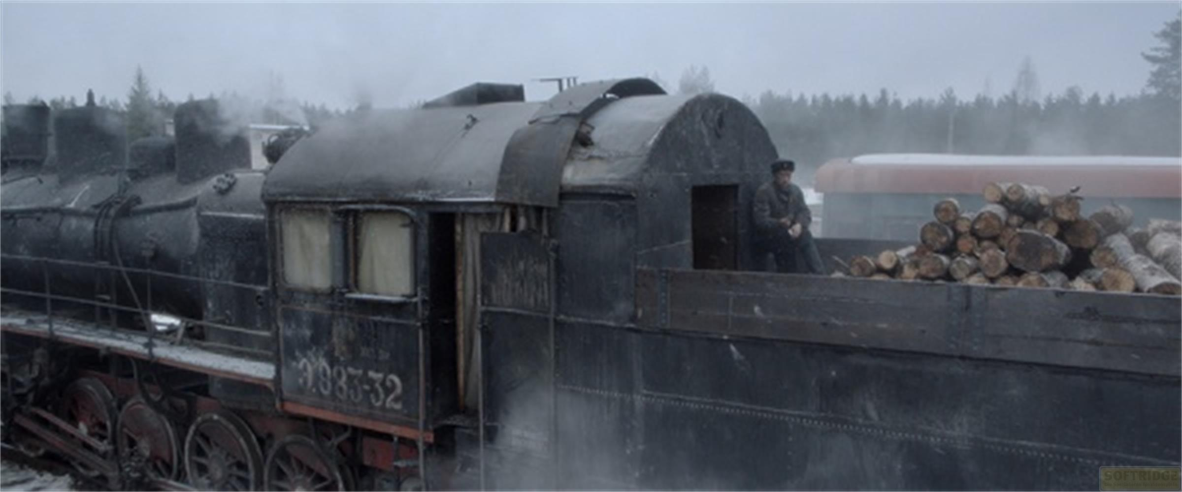 Un uomo seduto su una catasta di legna accanto a una locomotiva a vapore nella nebbia.