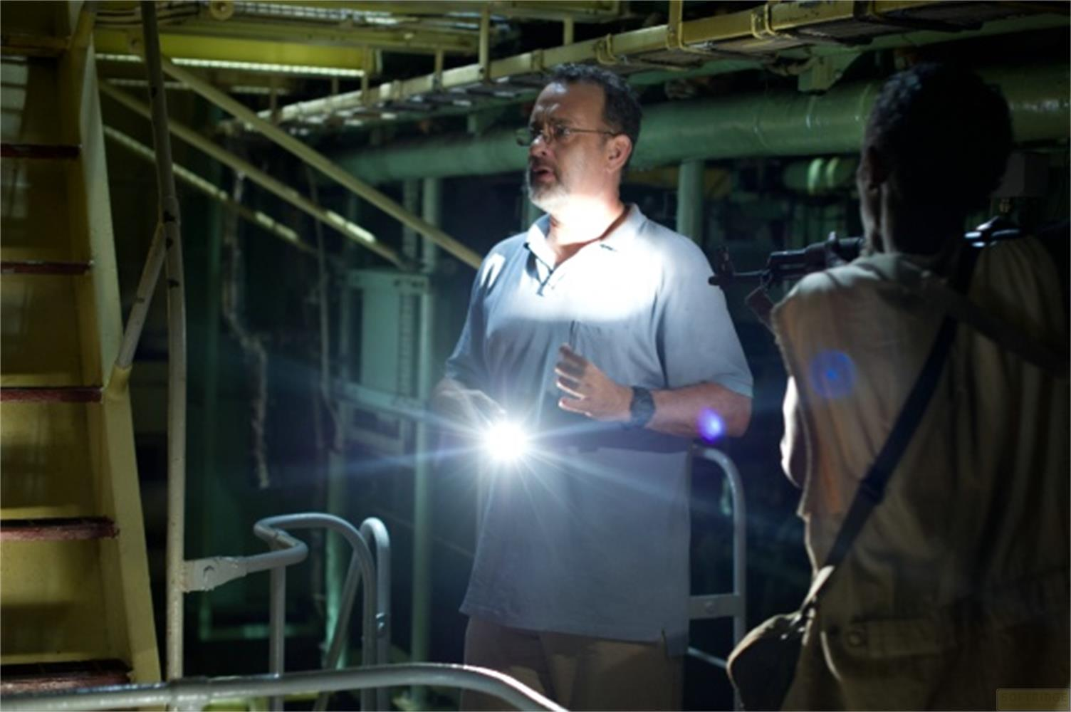 Un homme avec des lunettes éclaire avec une lampe de poche dans un cadre industriel sombre.