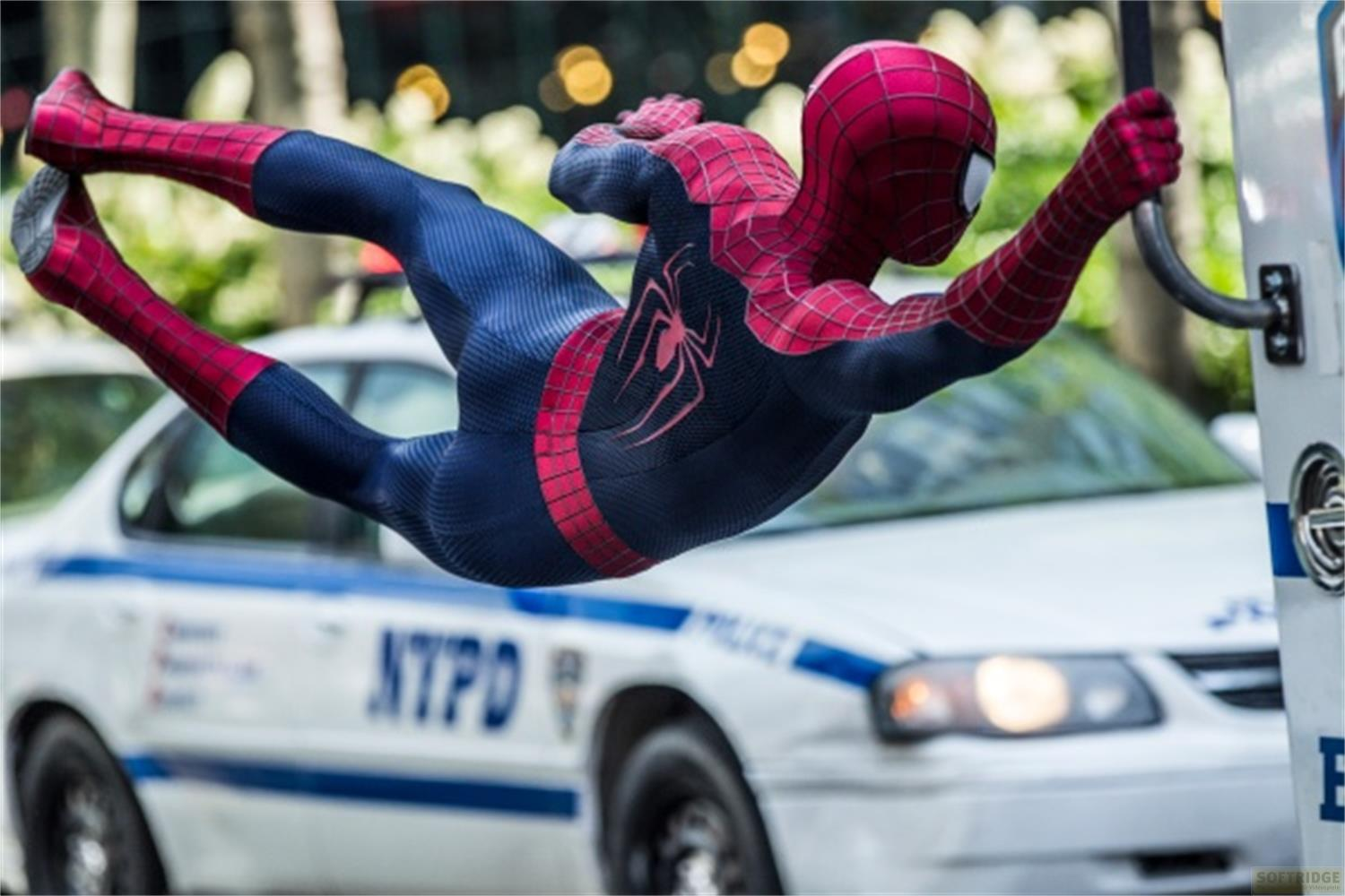 Spider-Man in Rot und Blau fliegt an einem NYPD-Auto vorbei.