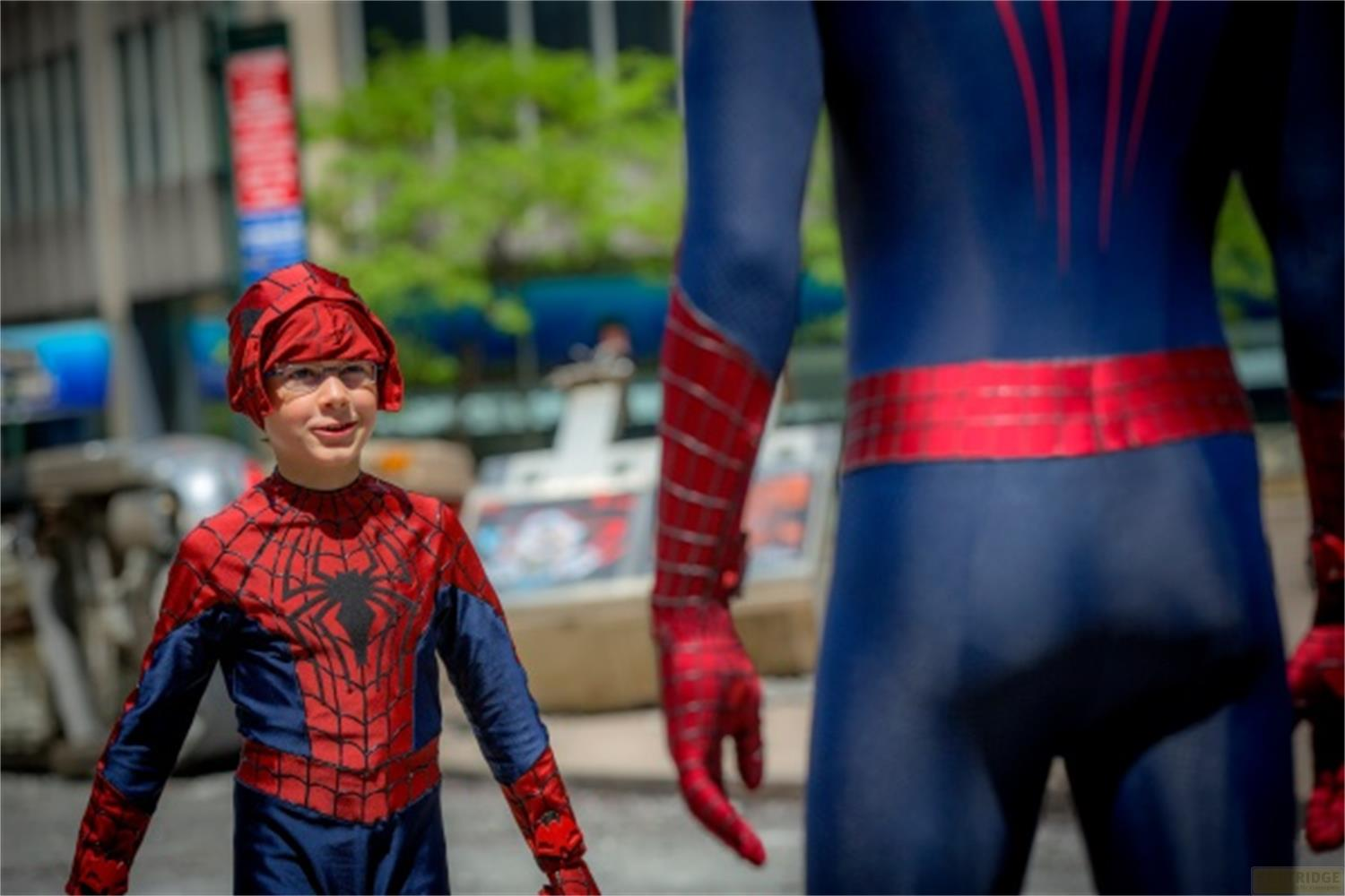 Ein Junge im Spiderman-Kostüm steht vor einer größeren Spiderman-Figur im Freien.