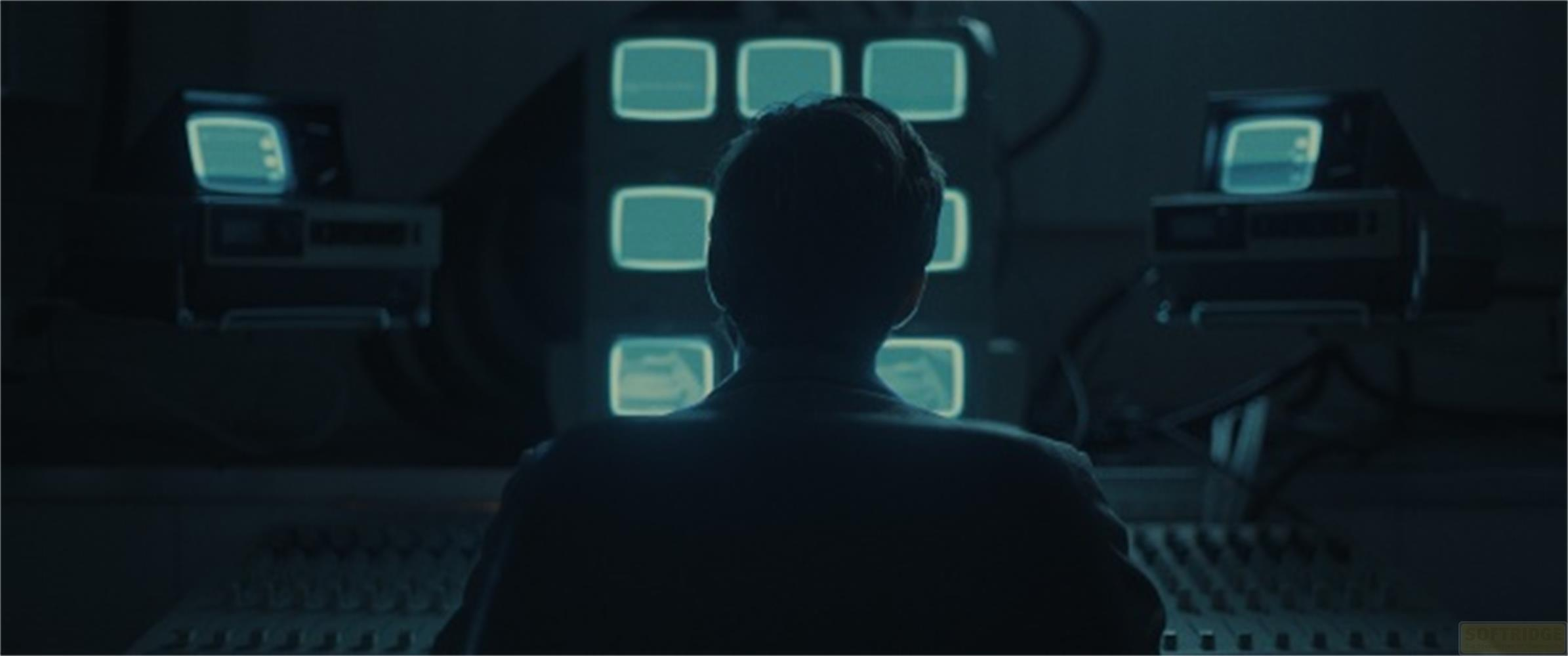 Silhouette di persona davanti a monitor e mixer in una stanza buia.