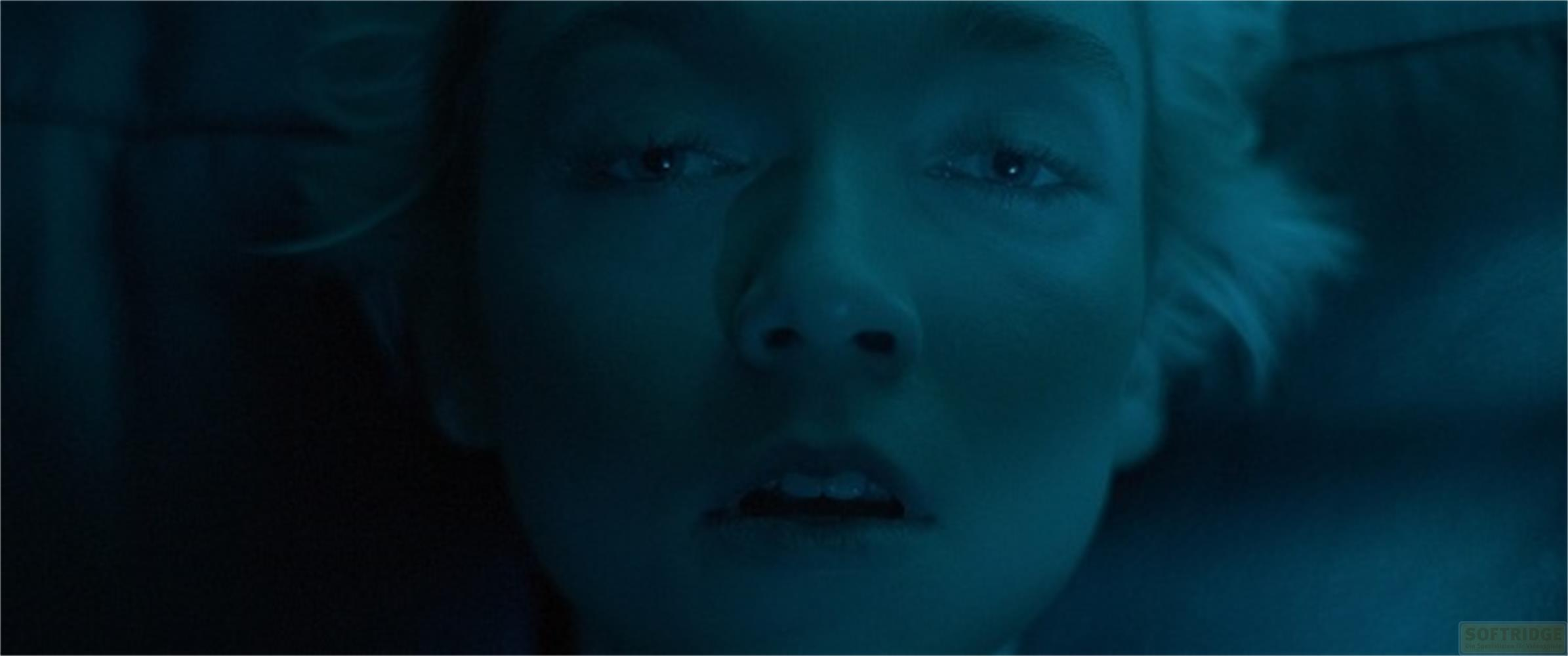 Primo piano di un viso in luce blu, occhi aperti, bocca socchiusa.
