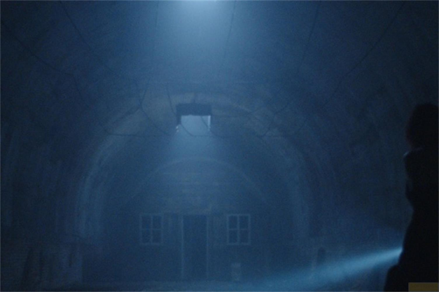 Un uomo con una torcia illumina un tunnel buio e nebbioso con un edificio.