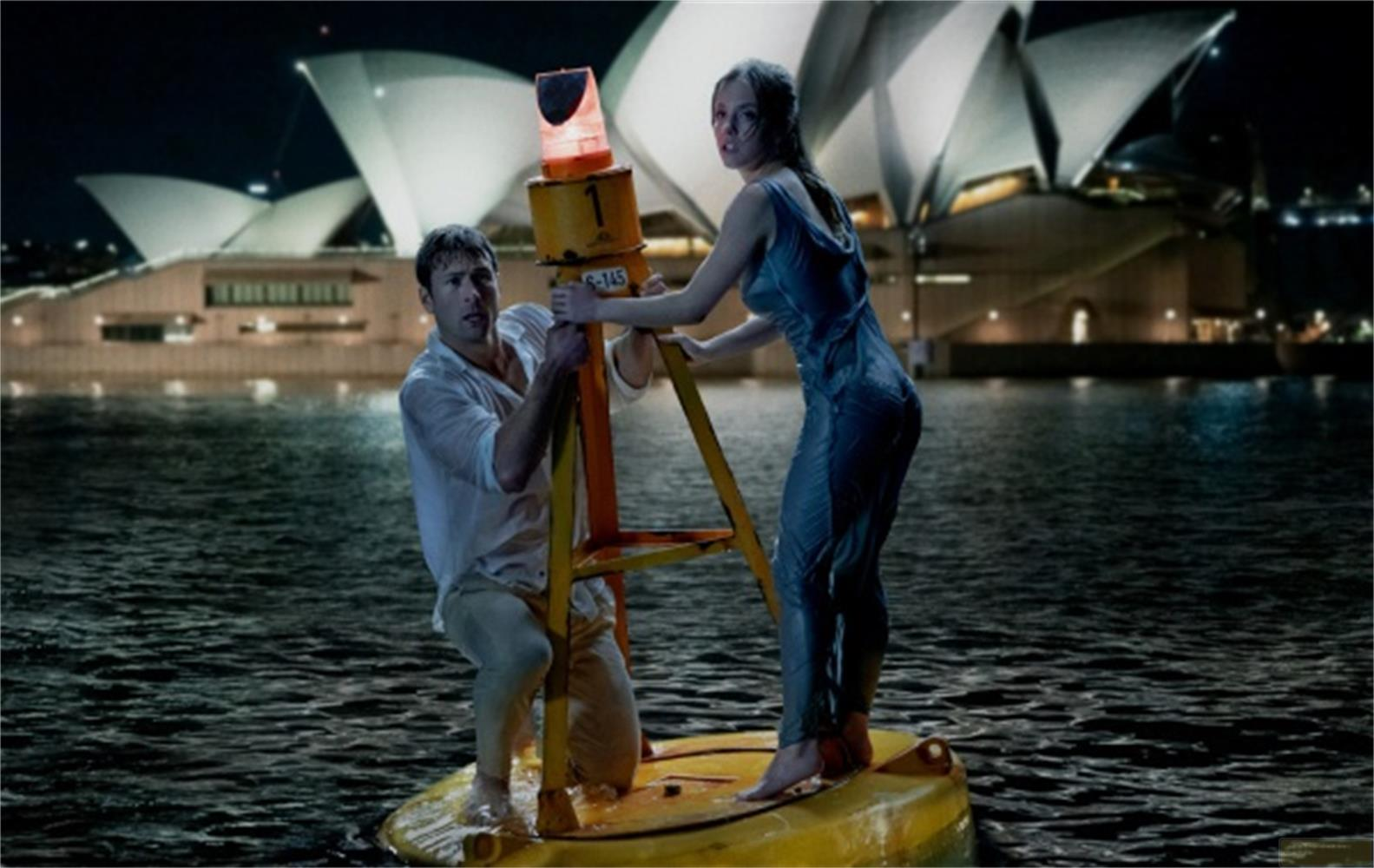Uomo e donna si aggrappano a una boa di notte, Opera di Sydney sullo sfondo.