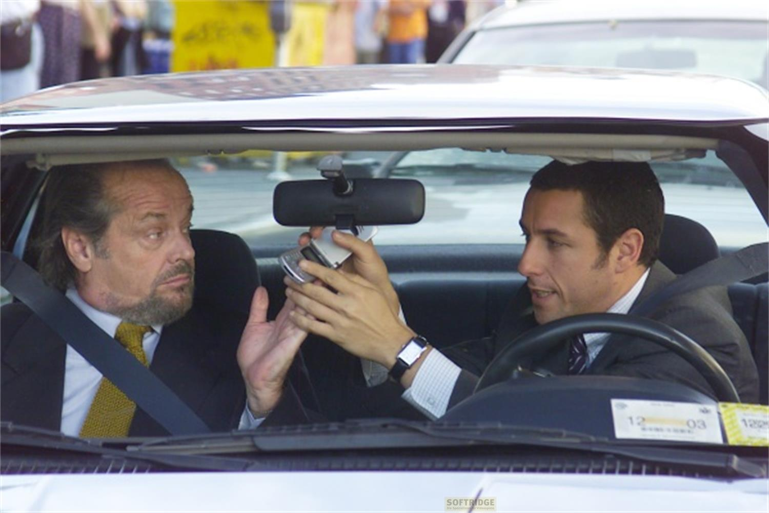 Deux hommes dans une voiture, l'un donnant un téléphone portable à l'autre.