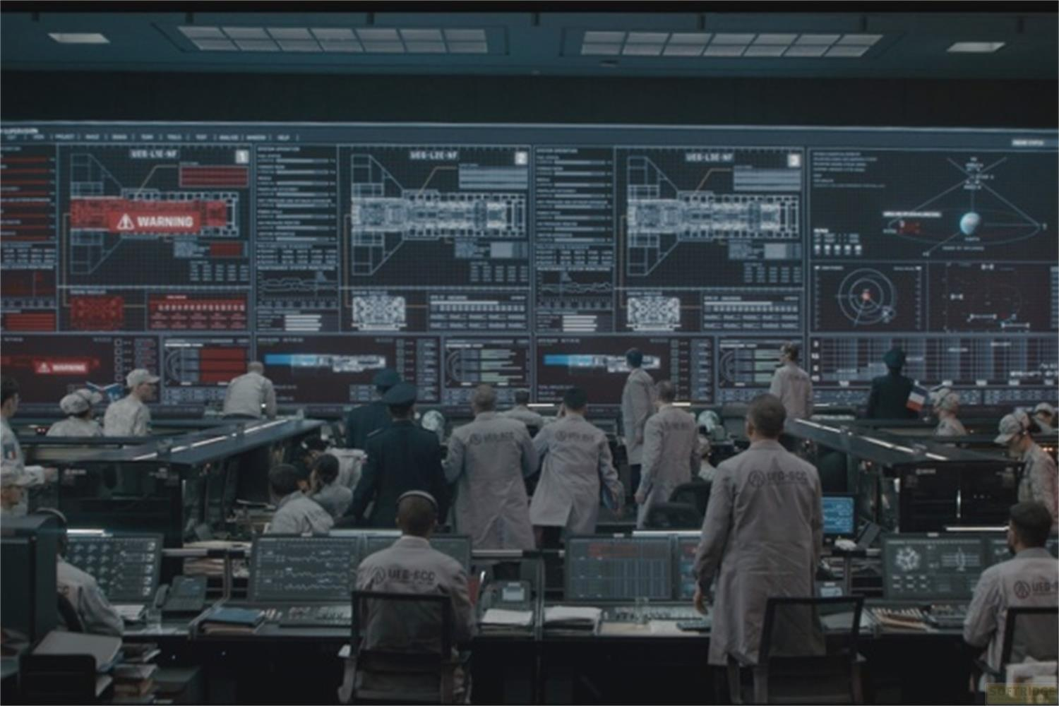 Persone in una sala di controllo davanti a grandi schermi che mostrano diagrammi e avvisi.
