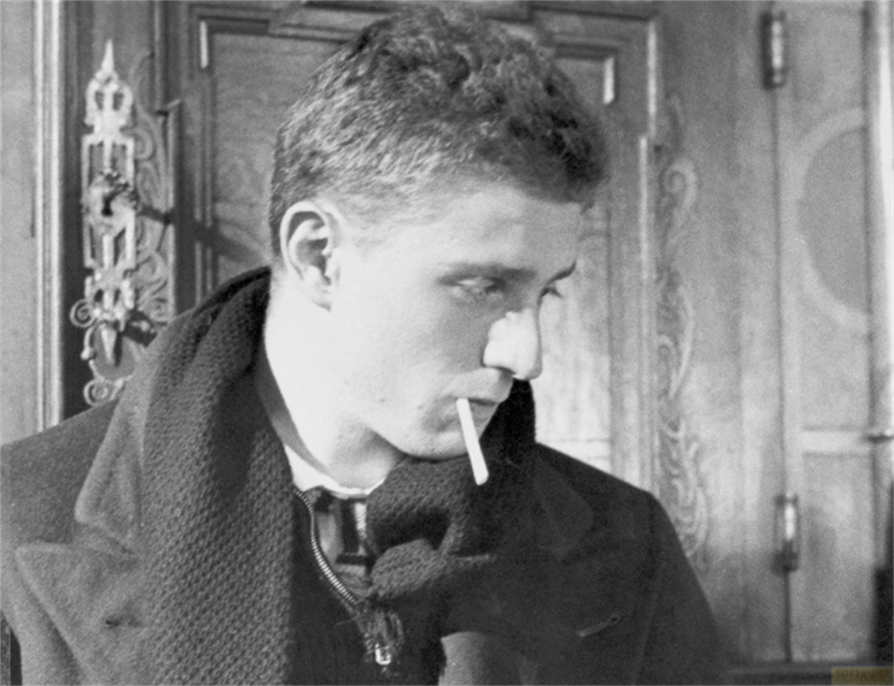 Giovane uomo con sigaretta in bocca, cappotto e sciarpa scuri.