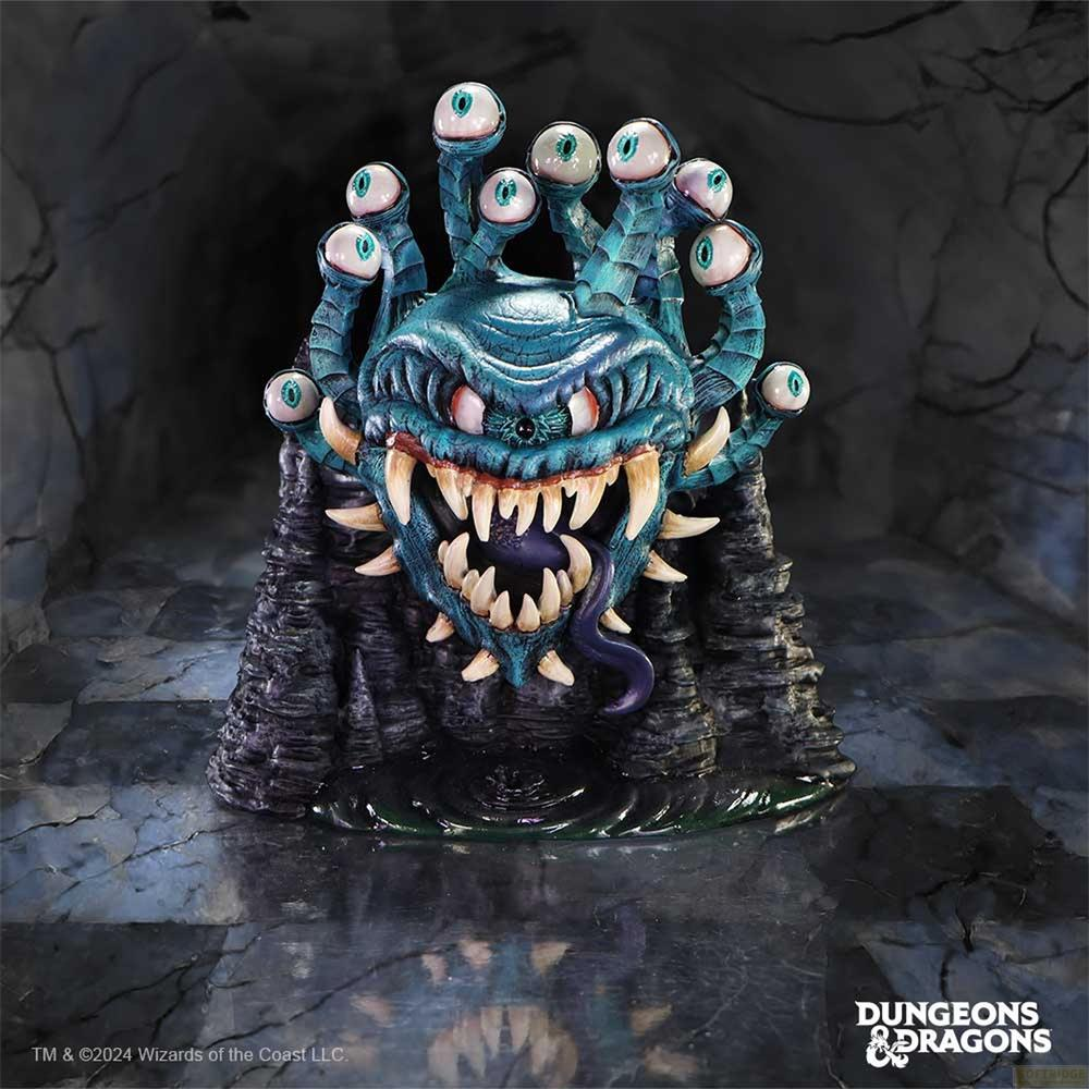Een blauwgroene beholder met vele ogen op stelen, gezeten op een rotsachtige basis.