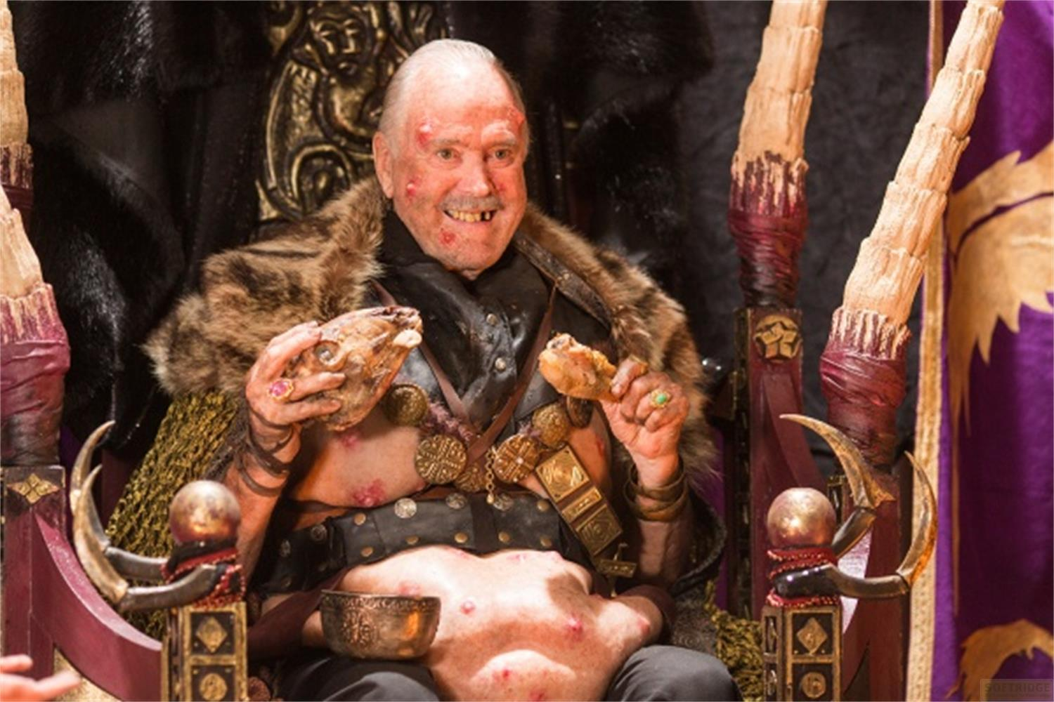Un uomo seduto su un trono mangia una testa d'animale e carne.