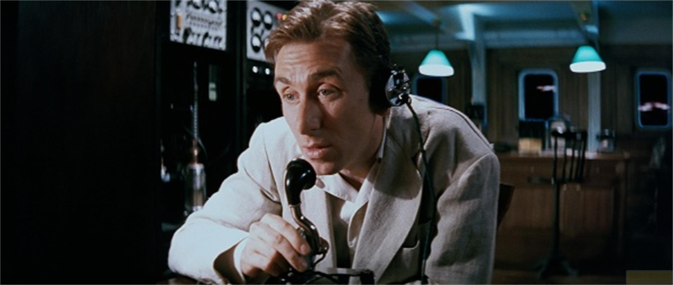 Un uomo con le cuffie parla in un vecchio telefono in una stanza con finestre.