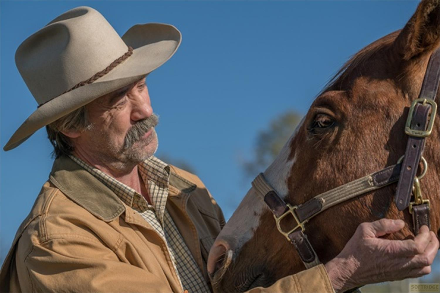 Un cowboy con cappello e baffi accarezza un cavallo.