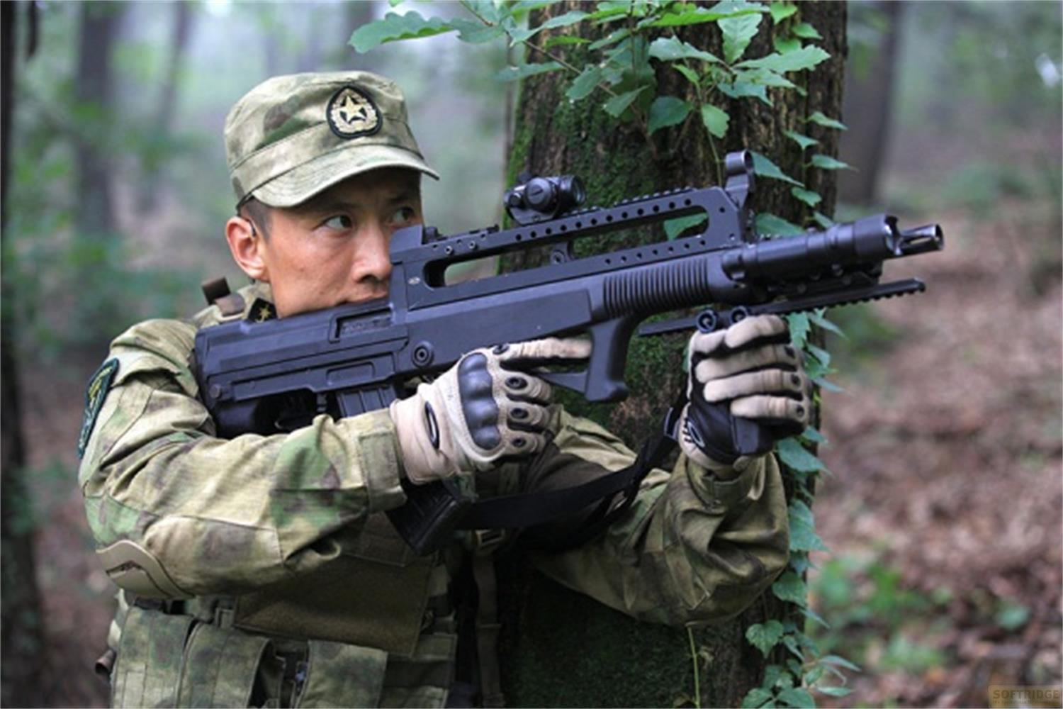 Soldat en uniforme de camouflage tient un fusil en forêt, arbre en arrière-plan.