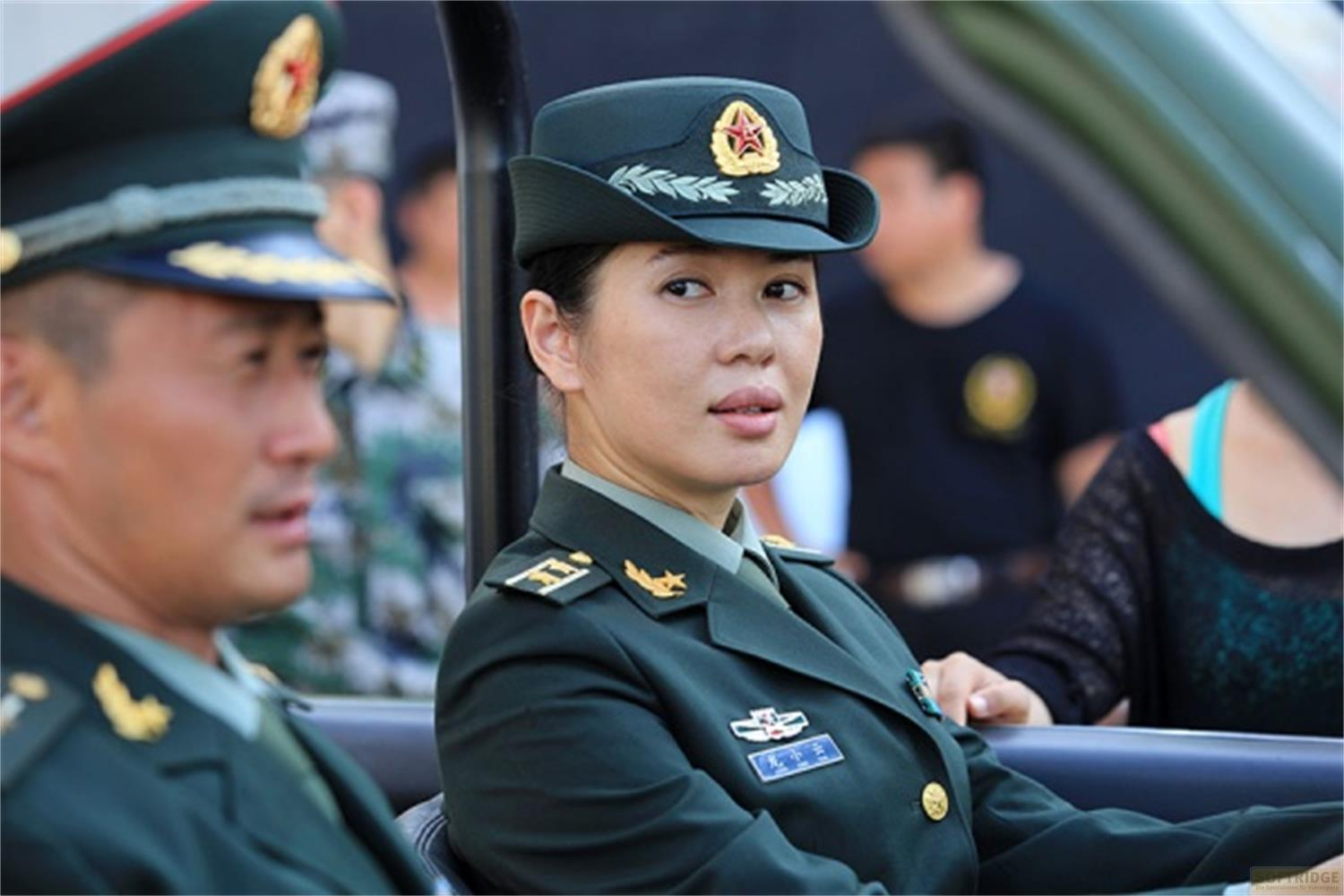 Deux militaires en uniforme sont assis dans un véhicule, une femme au premier plan.