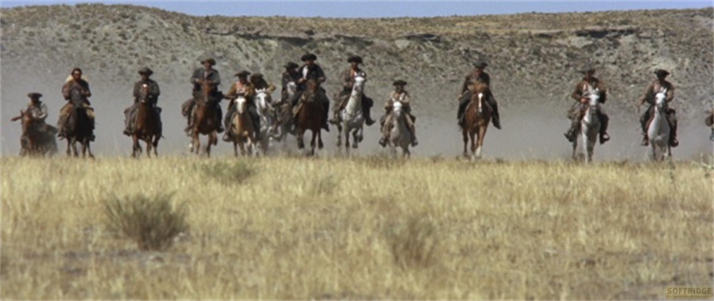 Un gruppo di cowboy a cavallo cavalca attraverso un paesaggio secco e collinare.