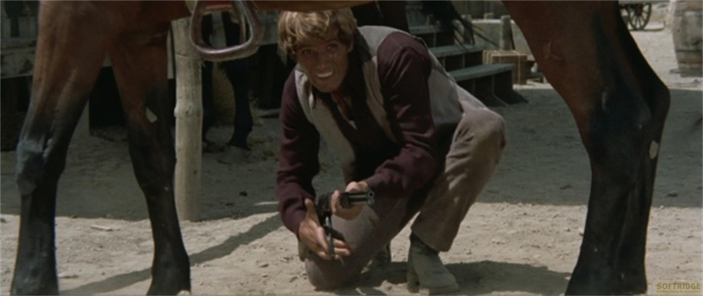 Un uomo in abiti western si inginocchia con una pistola accanto a un cavallo.