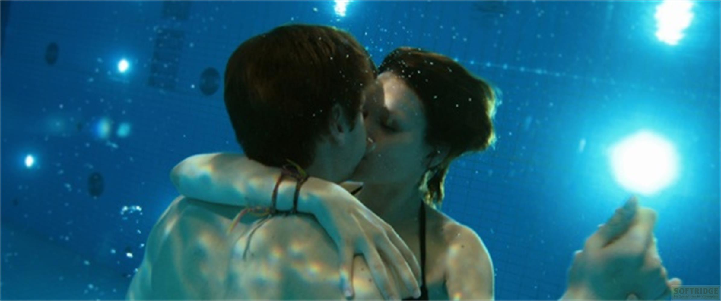 Una coppia si bacia sott'acqua in una piscina illuminata.