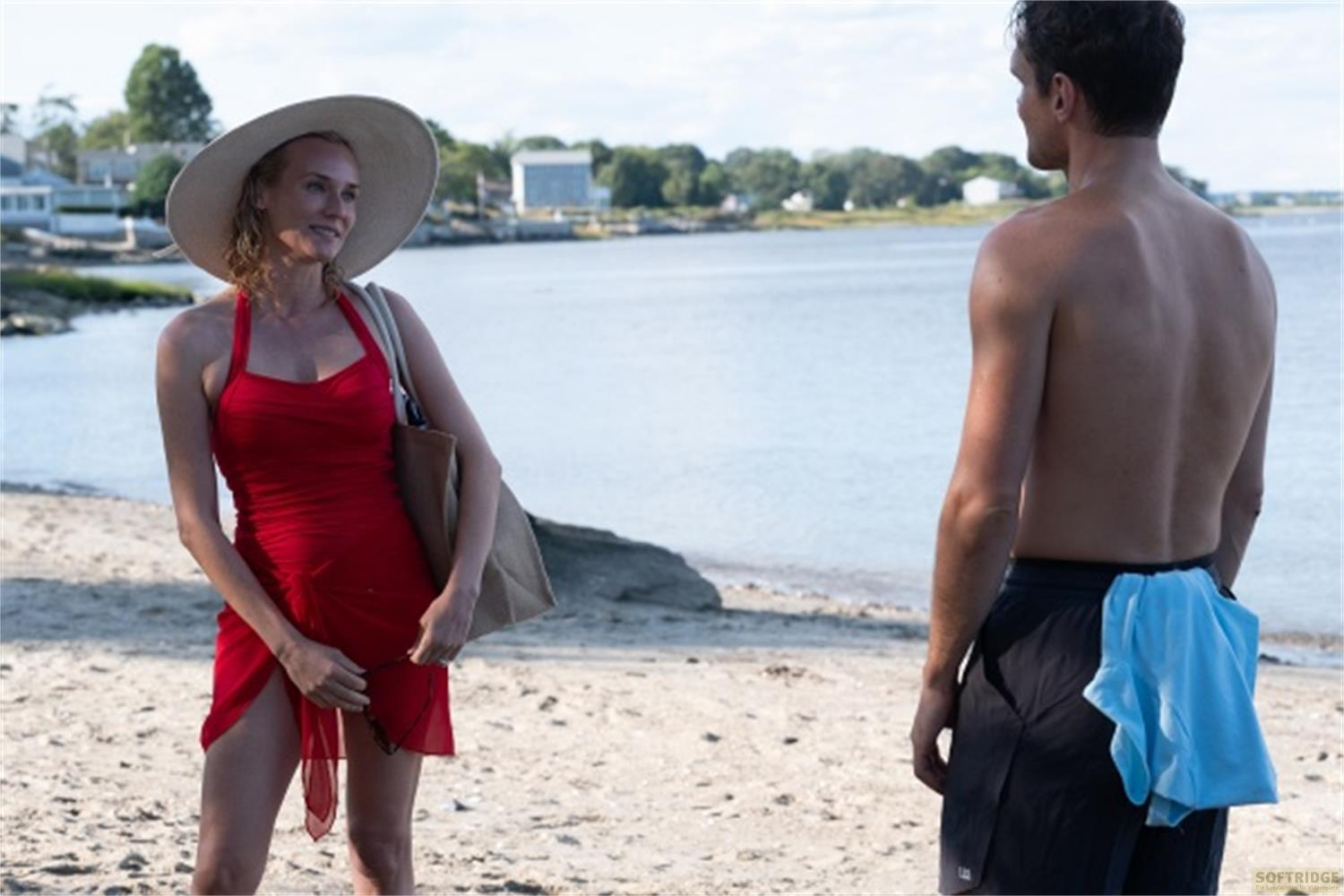 Una donna in abito rosso e cappello sulla spiaggia, un uomo sullo sfondo.