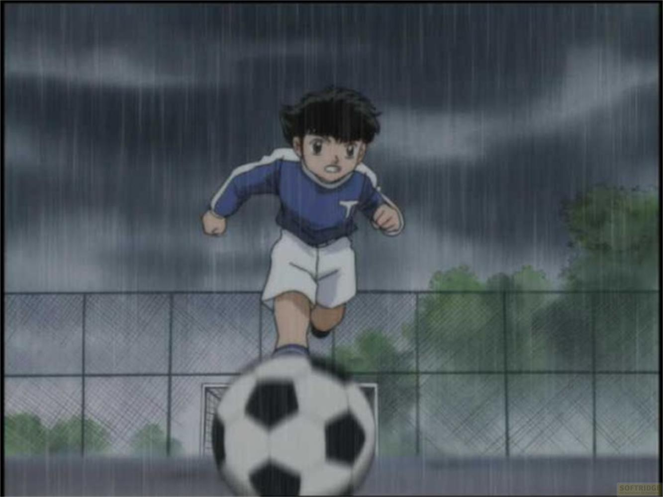 Un ragazzo in tenuta blu gioca a calcio sotto la pioggia.